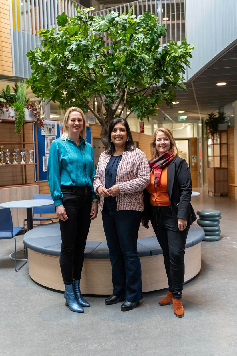 Drie vrouwen staan op de foto voor een boom in een gebouw.